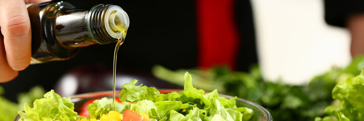 Cook holds bottle in hand and trickles olive extra virgin oil into fresh vegetable salad with vitamins. Raw food and vegetarian in modern society vegan is popular concept.