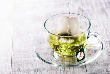 Pouring hot water to green tea. Hot green tea in beautiful glass cup on white table.