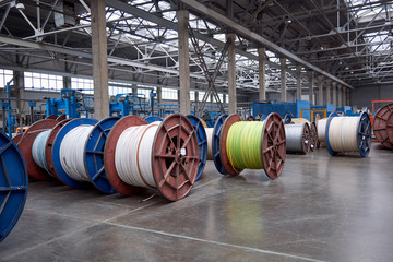 Several rows of large, heavy metal coils with electrical cables and wires in production. Modern line of automatic production of electric cable and wire. Coils on the concrete floor.