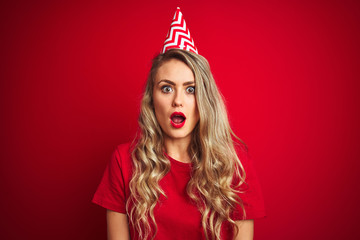 Young beautiful woman wearing bitrhday hat over red isolated background scared in shock with a surprise face, afraid and excited with fear expression