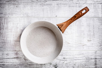 White frying pan on white rustic table.  Ceramic frying pan with beautiful wooden handle.