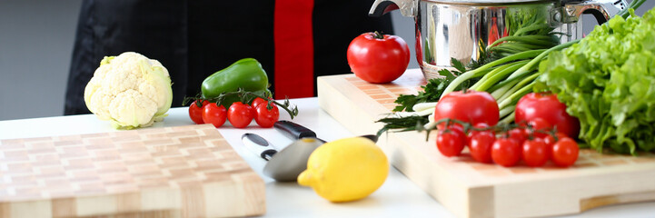 The cook in the kitchen is preparing to prepare a dish of fresh vegetables for a vegan, keeps his hands on his belt, the products lie on the table
