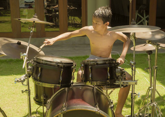 Fototapeta na wymiar Asian American teenager playing drums. Summer portrait of handsome young boy practicing on drum kit at home garden rehearsing rock song enjoying his hobby