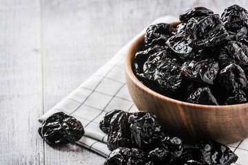 Prunes in wood bowl on white rustic table. Dried plums on white table. Fresh prunes for healthy life.