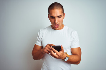 Young handsome man using smartphone over yellow isolated background scared in shock with a surprise face, afraid and excited with fear expression