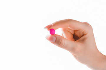 Fototapeta premium Hand holding red or pink pill on white background. Fingers holding pill close up isolated.