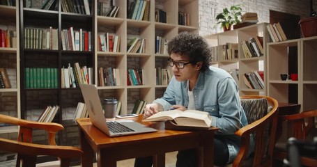 Asian student doing research in library using laptop in books, making a project and preparing for exam. Nerdy guy studying his lessons - education, self-study concept 4k close up - Powered by Adobe