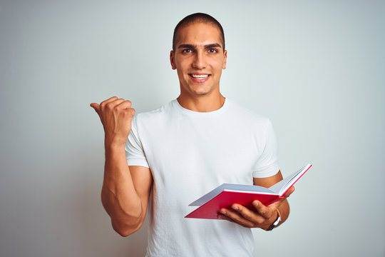 Young handsome man reading red book over white isolated background pointing and showing with thumb up to the side with happy face smiling