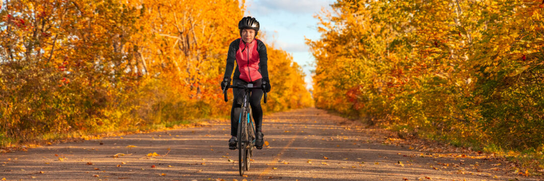 Biking cyclist cycling on road bike in autumn nature outdoor park. Asian girl cycling enjoying cold weather and foliage background panoramic banner.