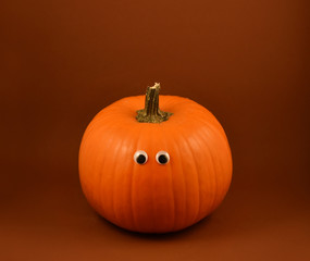Halloween pumpkin with googly eyes stock images. Halloween pumpkin with googly eyes on a brown background. Cute halloween pumpkin on a dark background
