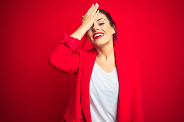 Young beautiful business woman standing over red isolated background surprised with hand on head for mistake, remember error. Forgot, bad memory concept.