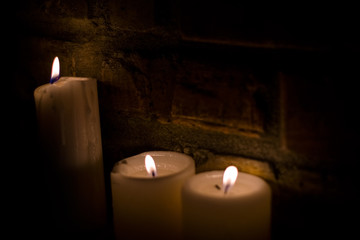 Background or texture of large white burning candles in dark room near brick wall. Holiday. Helloween.