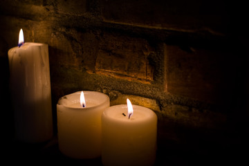Background or texture of large white burning candles in dark room near brick wall. Holiday. Helloween.