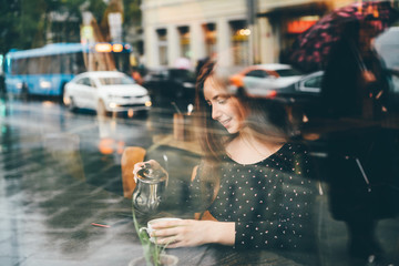 Woman drinking hot tea and looking at window in autumn sity in cozy restraunt. Concept of autumn...