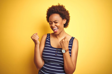 Beauitul african american woman wearing summer t-shirt over isolated yellow background very happy and excited doing winner gesture with arms raised, smiling and screaming for success