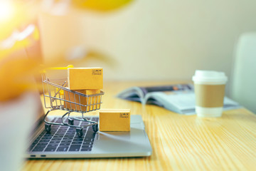 Brown paper boxs in a shopping cart with laptop keyboard on wood table in office background.Easy shopping with finger tips for consumers.Online shopping and delivery service concept.