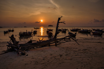 Fototapeta na wymiar Boat or Taxi moored in The beach in Thailand in the sunset of a summer day with sun and clouds. Also called Longtails.