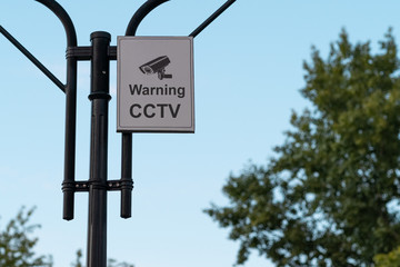 CCTV. warning sign. white sign on a metal pillar against a blue sky and treetops in a park