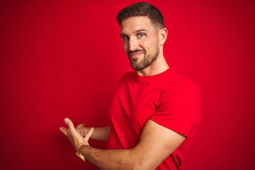 Fototapeta premium Young handsome man wearing casual t-shirt over red isolated background Inviting to enter smiling natural with open hand