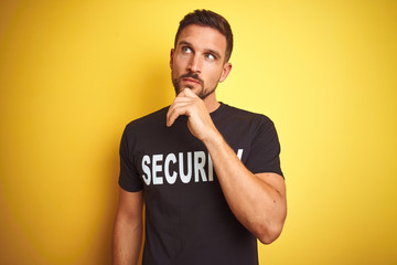 Young safeguard man wearing security uniform over yellow isolated background with hand on chin...