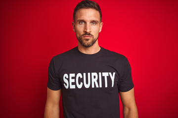 Young safeguard man wearing security uniform over red isolated background with serious expression...