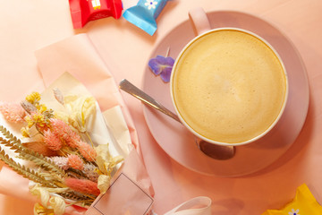 The cup of coffee with flowers and candys on the pink background