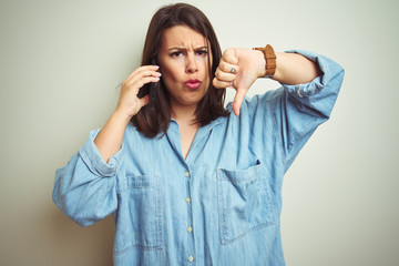Young beautiful woman having a conversation using smartphone over isolated background with angry face, negative sign showing dislike with thumbs down, rejection concept