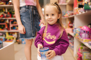 Adorable little girl with mom shopping for toys. Cute female in toy store. Happy young girl selecting toy