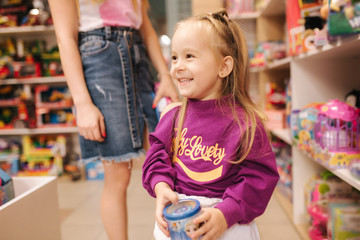 Adorable little girl with mom shopping for toys. Cute female in toy store. Happy young girl selecting toy