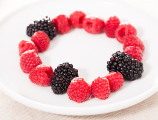 raspberries and blackberries laid out on a white plate in circle