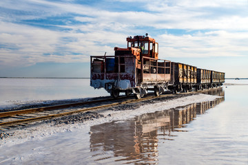 Awesome train rides on rail in the water with white salt on the background of beautiful blue sky.