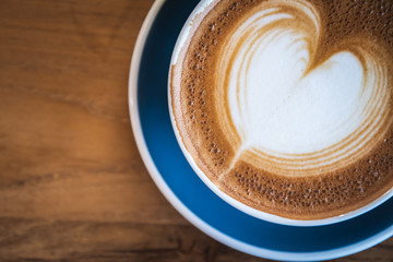 Close up of hot cappuccino coffee with latte art on wooden coffee table, selective focus for drink background