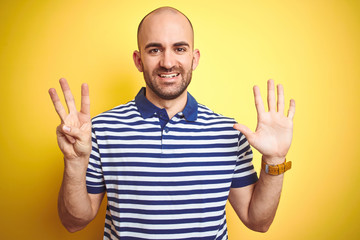 Naklejka premium Young bald man with beard wearing casual striped blue t-shirt over yellow isolated background showing and pointing up with fingers number eight while smiling confident and happy.