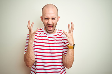 Naklejka premium Young bald man with beard wearing casual striped red t-shirt over white isolated background celebrating mad and crazy for success with arms raised and closed eyes screaming excited. Winner concept