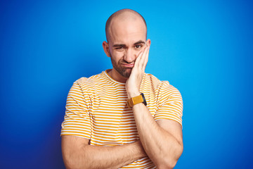 Young bald man with beard wearing casual t-shirt over blue isolated background thinking looking tired and bored with depression problems with crossed arms.