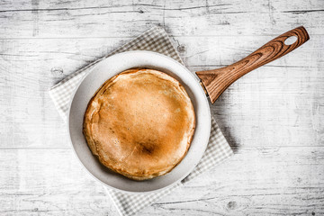 Frying white pancake pan with baked pancake on white rustic table.