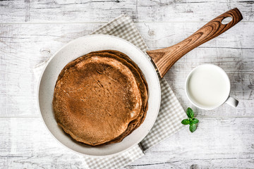 Frying pan with pancake and jar of milak with green mint leaf on white old table. Pancakes in frying pan.