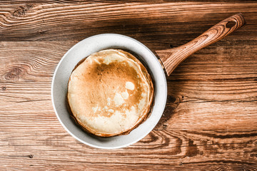 White frying pan on wooden rustic table with pancakes. Pancakes in frying pan.