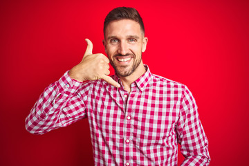 Fototapeta premium Young handsome man over red isolated background smiling doing phone gesture with hand and fingers like talking on the telephone. Communicating concepts.