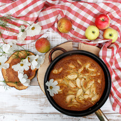 Pie with Apple on the wooden white background with a red tablecloth and flowers of cosmos. The concept of home food, healthy nutrition, comfort, warmth. Rustic style of life.