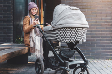Woman with baby stroller walking,sitting on bench, using smartphone for online communication.Girl...