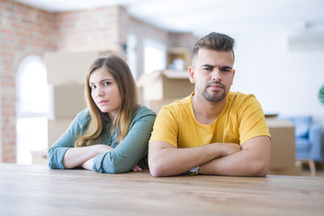 Young couple sitting on the table movinto to new home with carboard boxes behind them skeptic and nervous, disapproving expression on face with crossed arms. Negative person.