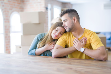 Young couple sitting on the table movinto to new home with carboard boxes behind them smiling with...