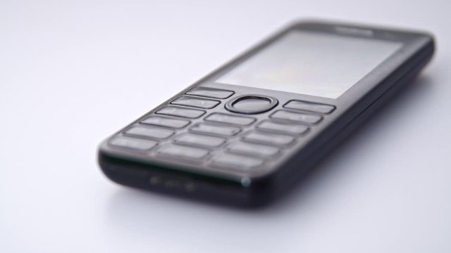 Old school keypad button black mobile phone on a white background, sliding shot