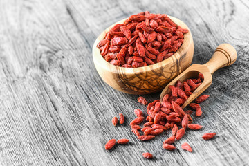 Goji in wooden bowls with green leaves. Goji in scoop. Pile of goji on table.