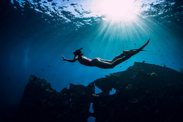 Free diver girl in pink swimwear with fins swimming underwater at wreck ship. Freediving in the...