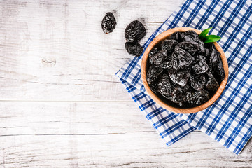 Fototapeta na wymiar Fresh dried prunes in wood bowl on blue cloth and white old rustic table. Dried plums on table. Fresh prunes for perfect health.