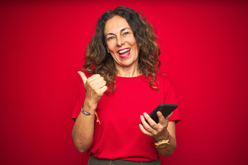 Naklejka premium Middle age senior woman using smartphone over red isolated background pointing and showing with thumb up to the side with happy face smiling