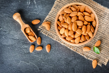 Top view of almonds on dark stone talbe with wooden spoon or scoop. Almonds in wooden bowl. Almonds laid freely on dark table.