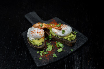 Poached eggs with bacon on toasts. Laid out on black slate.